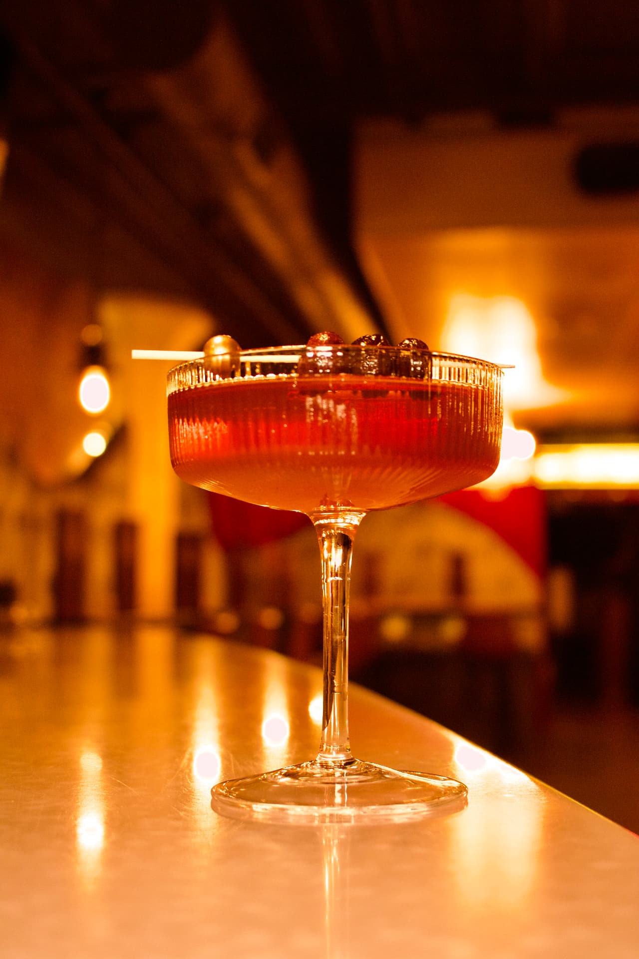 A ruby cocktail in a fluted coupe glowing on the Society bar top
